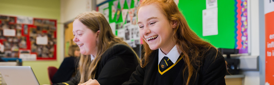 Female students working at laptops and laughing