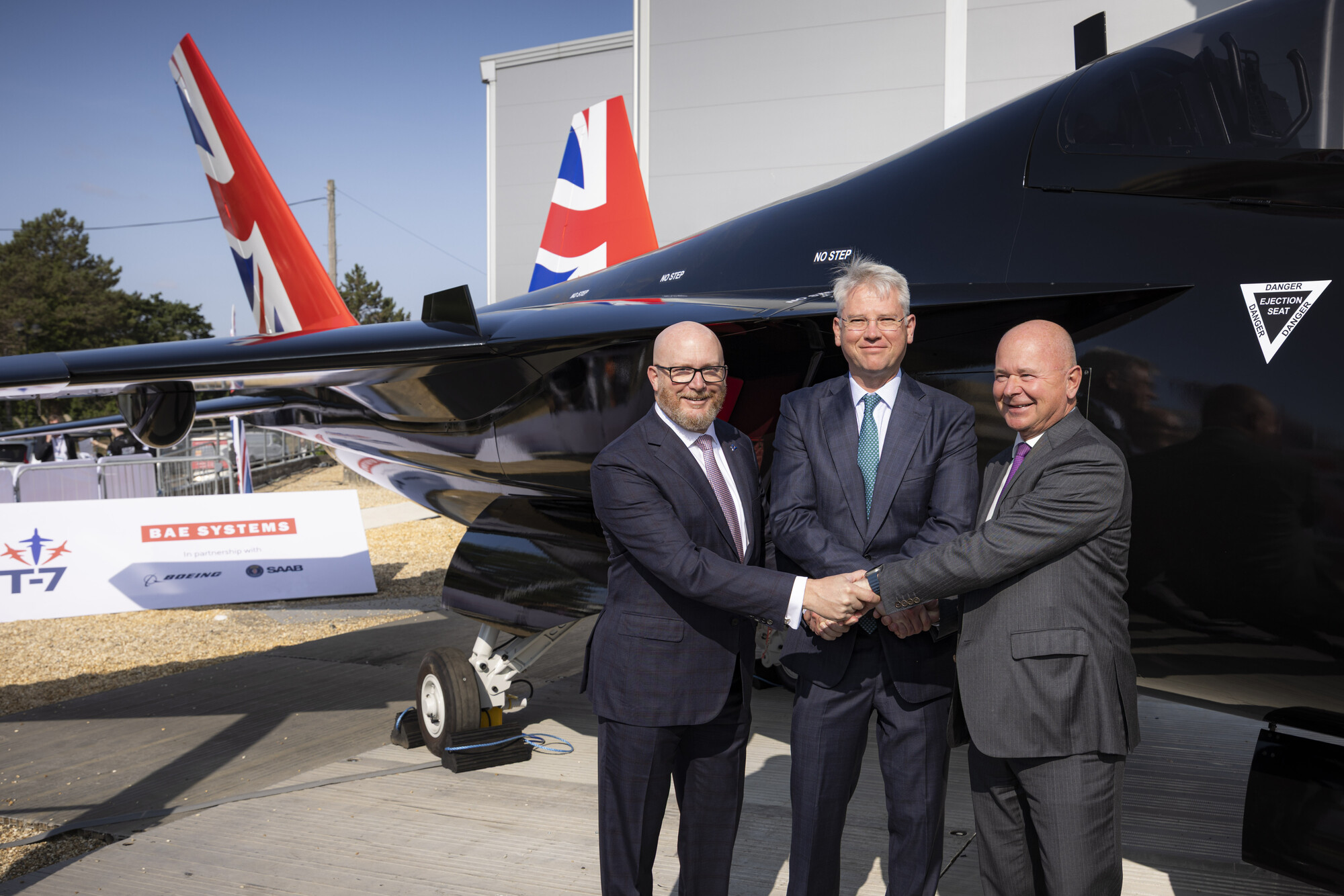 (L-R) Boeing Defense, Space & Security President and CEO Steve Parker, BAE Systems Chief Executive Charles Woodburn, and Saab President and CEO Micael Johansson shake hands at the Farnborough Airshow beside BAE Systems’ full-scale replica of the Boeing T-7. The three companies have formalised a teaming agreement to develop a next-generation pilot training system for the UK. (© BAE)