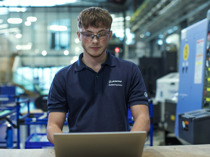 A male factory worker wearing safety glasses using a laptop